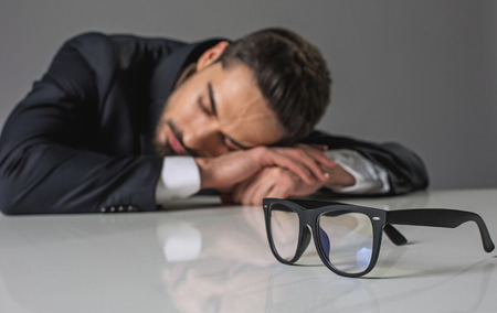 Focus on glasses. Sleeping overworked businessman in suit lying on white table and sleepingの写真素材