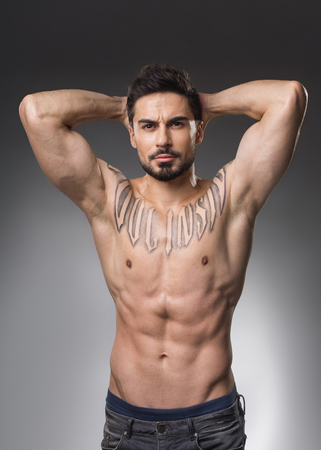 Waist up portrait of serious muscular man with naked upper body holding hands on back of his hand. Isolated on backgroundの写真素材