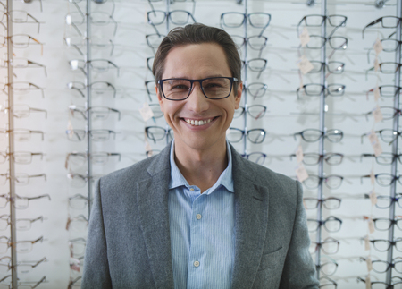 Portrait of beaming man in spectacles looking at camera while standing in optician shop. Visitor buying spectacles conceptの写真素材