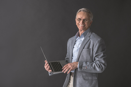 Portrait of outgoing senior male typing in notebook computer while holding it in hand. Technology conceptの写真素材