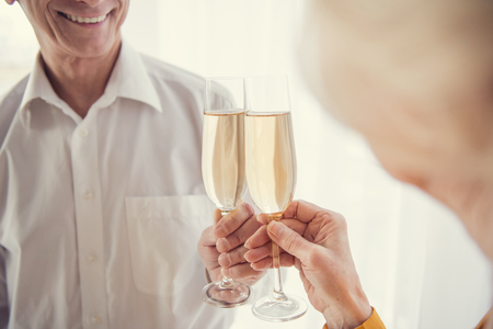 Smiling senior man clinking glasses of wine with aging woman standing in front of himの写真素材