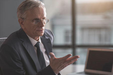 Portrait of focused old businessman gesticulating arms while locating indoor. Profession conceptの写真素材