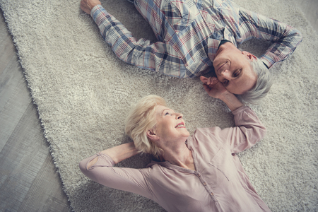 Top view of satisfied senior couple resting on comfortable rug and looking at each other with affectionateness. Woman running her hand over male faceの写真素材