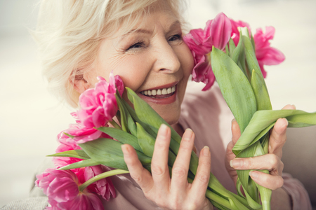 Portrait of delighted gray haired granny holding beautiful tulips close to her face and laughingの写真素材