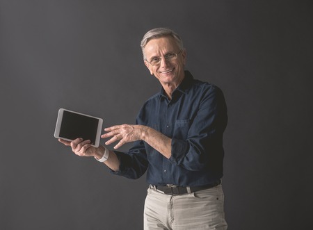 Portrait of beaming senior male demonstrating screen of digital device while keeping it in hand. Presentation of technology conceptの写真素材