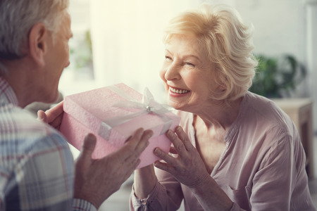 Senior female person with satisfied face taking present box which husband passing herの写真素材