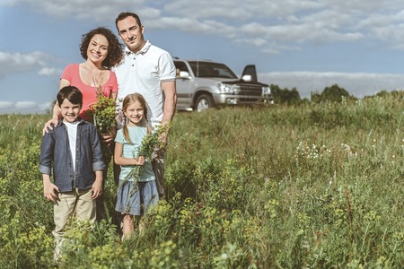 Happy together. Full length portrait of cheerful father and mother spending time with their kids on grassland. Girl is holding bouquet of wild flowers while boy is smiling. Copy spaceの写真素材