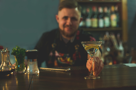 Portrait of smiling unshaven barman giving appetizing alcohol liquid. Happy man during occupation in club conceptの写真素材