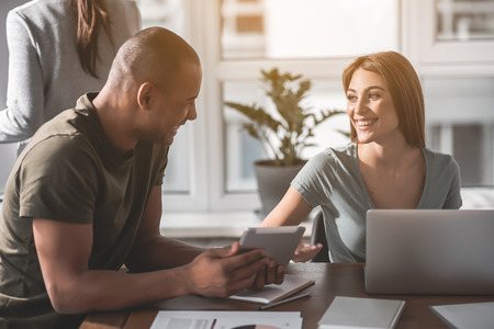Male and female people talking with joy at the table. Guy showing tabletの写真素材