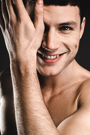 Outgoing man with brilliant smile closing eye by hand. Cheerful dude covering eye concept. Close upの写真素材