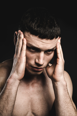 Portrait of miserable male stripped to waist while feeling pain. He keeping head by arms. Distressed guy conceptの写真素材