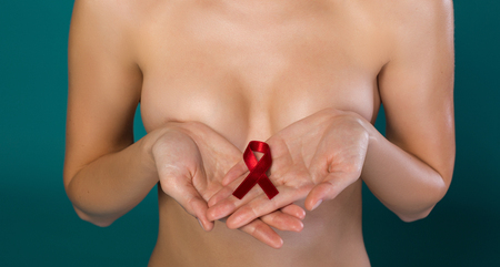 Close up of female hands holding red ribbon as a fight against breast cancer sign. Woman is standing...