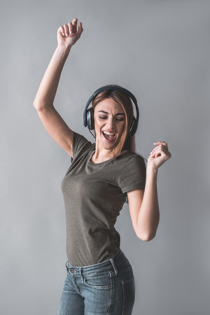 Portrait of young beautiful girl enjoying melody in her headphones. She is dancing and singing. Isolated on backgroundの写真素材
