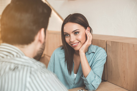 Romantic date. Portrait of charming young woman looking at man with love. She is sitting at desk and smilingの写真素材