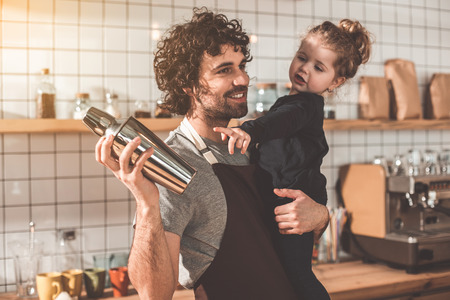 My daddy job. Cheerful man is looking after his little daughter while shaking beverage in cafeteria. Girl is pointing finger at shaker with interestの写真素材