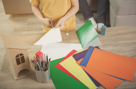 Top view close up of boy hands cutting paper by scissors. Focus on colorful carton on deskの写真素材