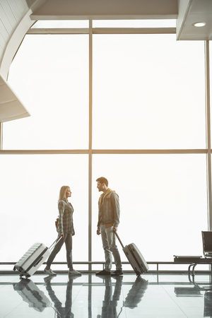 Full length side view beaming woman speaking with outgoing male in airportの写真素材