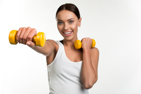 Endurance concept. Portrait of enjoyed lady holding dumbbells in arms. Focus on hand with equipment. Isolated on backgroundの写真素材