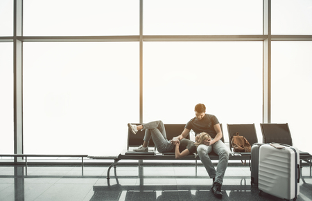 Full length cheerful lady lying on legs of smiling young male in lounge zone in airport. Glad couple resting during waiting of plane concept. Copy spaceの写真素材