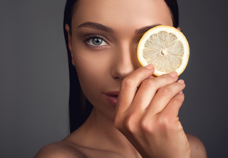 Close up of good looking female person covering her eye with orange cut and looking at camera. Isolated on backgroundの写真素材