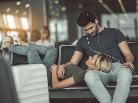Smiling woman looking at cheerful male while talking with him. He listening music with headset. Glad couple during rest conceptの写真素材