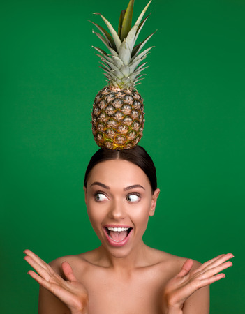 Portrait of naked girl with astonished expression keeping pineapple on the top of her head. Isolated on backgroundの写真素材