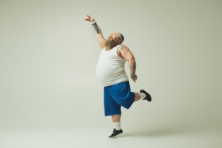 Feeling like a bird. Inspired fat man is dancing with grace and serenity. He is raising hand up while standing on one legの写真素材