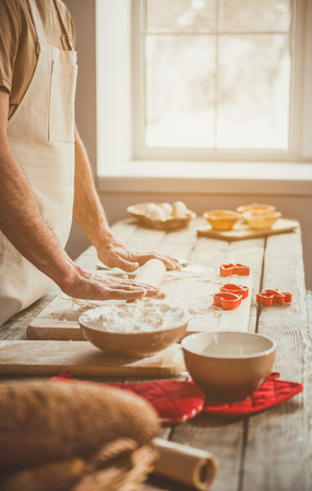 Adult guy unrolling soft pastry for carving cookies. Window on background. Close upの写真素材
