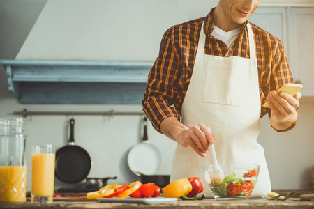 Male cook preparing healthy salad and looking at mobile phone in his hand. Copy space in left sideの写真素材