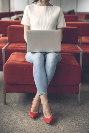 Woman having job with laptop while sitting on cozy armchair in lounge zoneの写真素材