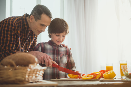 Father and son holding one knife for two and slicing bell peppers. Copy space in right sideの写真素材