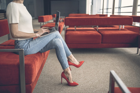 Woman in modern red shoes having labor with notebook computer while resting in lounge zoneの写真素材