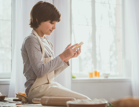Side view profile of little boy relaxing on desk with smartphone in hands. Ingredients and inventory...