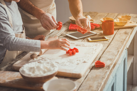 Man and boy working with knead indoors. They doing cookies with cutters in their hands. Close upの写真素材