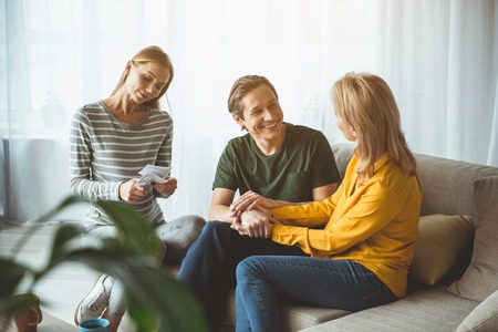 Excited future parents are sitting on sofa and smiling. Pregnant woman is looking at ultrasound pictures of her baby with gentleness. Surrogate motherhood conceptの写真素材