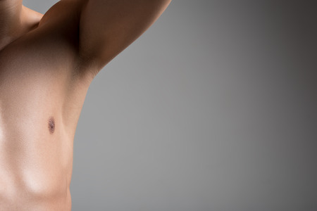 Close up half of torso of young man with smooth armpit. He is standing with raised arm against light wall and demonstrating his hairless underarm. Laser hair removal concept. Copy space in right sideの写真素材