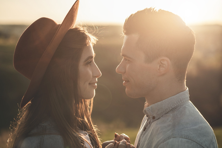 Close up of man and female in love holding hands. They are looking at each other with smiles and care during sunset in natureの写真素材