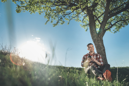 Feeling relaxed. Full length of handsome smiling man sitting with cellphone and earphones. He is looking far away with joy and excitement. Copy space in left sideの写真素材