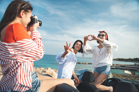 Best memories. Pleasant cute young woman is holding camera and taking photos of her female friends...