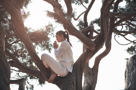 Profile of relaxed young woman doing meditation in the nature. She is joining palms together. Her eyes are closed with peace and serenityの写真素材