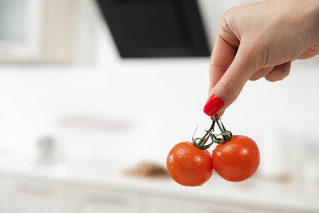 Close up of female hand holding two red tomatoes. Kitchen is on background. Copy space の写真素材