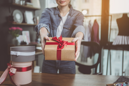 Close up woman arms demonstrating gift wrap with beautiful red ribbon for cameraの写真素材