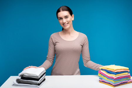 Waist up portrait of joyful housewife with two piles of folded fresh clothes. Happy female is...