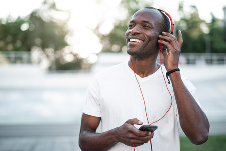 Portrait of beaming man with attractive smile hearing song after good training on open air. He...