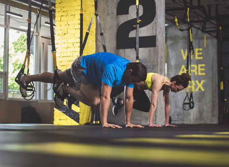 Full length side view orderly male and concentrated woman doing workout with suspension cableの写真素材