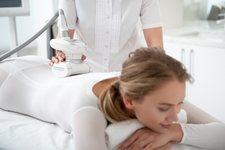 Woman hand making treatment procedure with gadget for young smiling female client in spa centerの写真素材