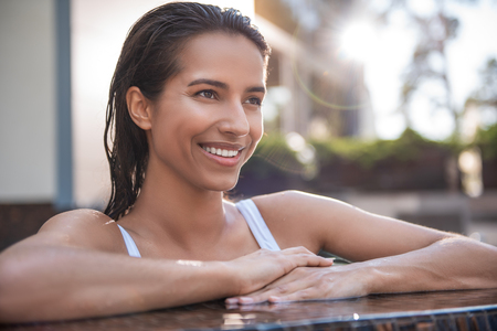 Portrait of cheerful woman with attractive smile resting on open air. Her hair is wet. She locating...