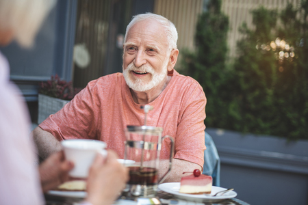 Waist up portrait of smiling senior male sitting at table and drinking tea with woman. They are having great time together in cafe outdoorsの写真素材
