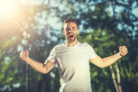 Waist up portrait of screaming man standing outside with stretched hands and smiling. He is enjoying sport and physical activity outsideの写真素材
