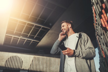 Low angle of happy man standing outside and communicating on smartphone with smile. He is pleased...